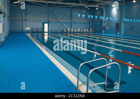 Sport Schwimmbad innen, niemand. Leerer Pool mit Gleisen und Leiter, blaues Wasser und Fliesen, öffentlicher Platz für gesunde Lebensretteln Stockfoto