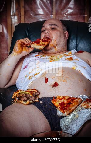 Fat couch potato Essen einer riesigen Hamburger und Fernsehen. Grelle Beleuchtung aus dem Fernsehen beleuchtet die dunklen Zimmer. Stockfoto