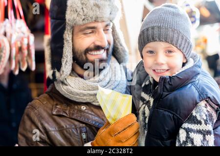 Vater und Sohn essen süß geröstete Mandeln auf dem Weihnachtsmarkt Stockfoto