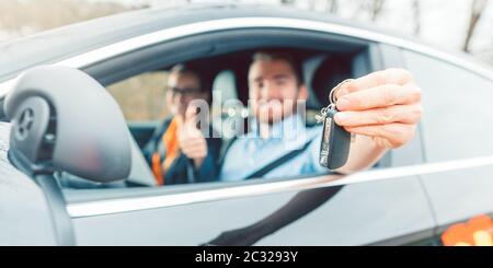 Schüler der Fahrschule, die seinen letzten Test bestanden hat und die Autoschlüssel aus dem Fenster zeigte Stockfoto