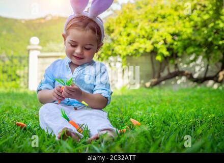 Kleiner Junge mit Freude an den Osterfeiertagen, mit lustigen, gruseln Hünenohren, der sonnige Tag auf dem Hinterhof genießt, glücklicher Frühlingsurlaub Stockfoto