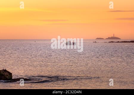Kleines Fischerboot, das den Hafen verlässt. Fliegende und schwimmende Möwen, die Boot abschrocken. Erstaunliche goldene Stunde su Stockfoto
