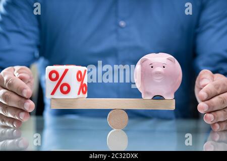 Die schützende Hand Balance zwischen Rot Prozentsatz kubische Block und Sparschwein auf hölzernen Wippe Stockfoto