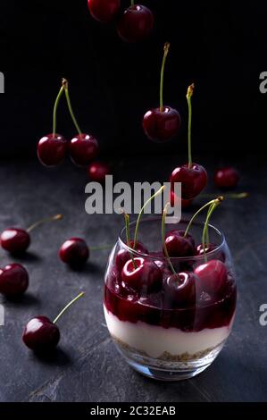 Geschichteter Kirschkäsekuchen in einem Glas. Dessert aus Keksen, Ricotta, Sahne, Kirschgelee und frischen Früchten. Dunkle launische Foto. Stockfoto