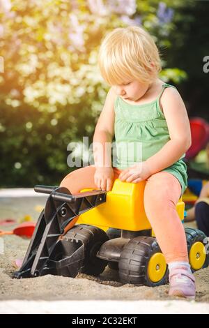 Mädchen Kind Reiten auf einem gelben Spielzeug Traktor auf dem Spielplatz Stockfoto