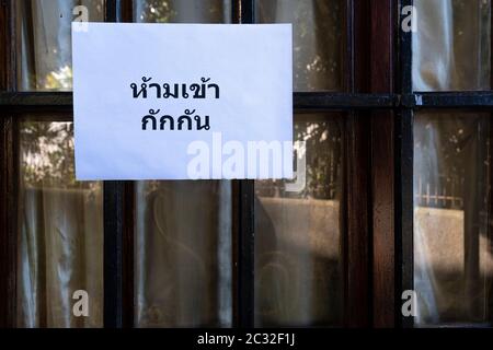 Ein Schild mit der Aufschrift "nicht eingeben", "Quarantäne in thailändischer Sprache", das an ein Fenster angehängt ist Stockfoto