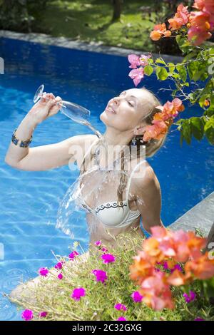 Schöne schlanke Frau in einem offenen Badeanzug im Pool gießt sich ein Glas Sekt. Sh