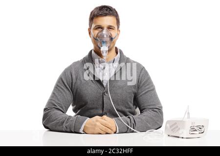 Junger Mann, der auf einem Tisch sitzt und eine Inhalationsmaschine benutzt, die auf weißem Hintergrund isoliert ist Stockfoto