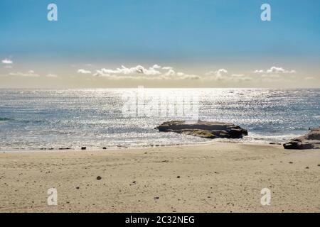 Strandabschnitt mit ruhigem silbernem Atlantik im Gegenlicht mit einem großen Lavastein am Wasserrand auf der Kanarischen Insel Teneriffa. Konzentrieren Sie sich auf Th Stockfoto