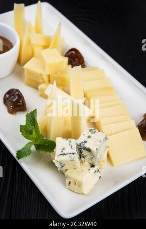 Käseplatte auf dunklem Hintergrund. Viele Arten von Käse mit Soße und Gruene haben sich auf eine weiße Platte, closeup Schuß Stockfoto