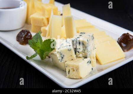 Käseplatte auf dunklem Hintergrund. Viele Arten von Käse mit Soße und Gruene haben sich auf eine weiße Platte, closeup Schuß Stockfoto