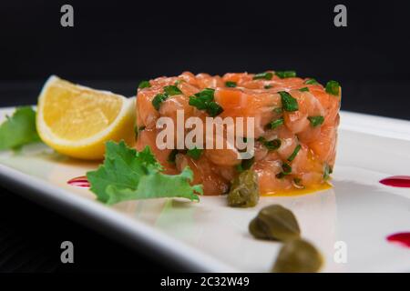 Frisches Lachstatar mit Kalk und Kapern auf weiße Platte Stockfoto