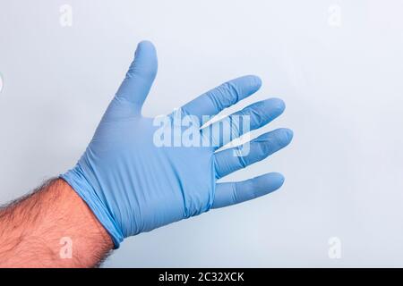 Hand des Arztes in einem blauen medizinischen Handschuh über hellblauem Hintergrund. Stockfoto