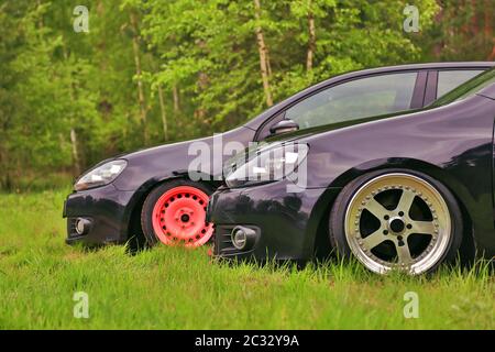 2 schwarze Autos im Tuning. Auf Gras geparkt. Mit benutzerdefinierten polierten Rädern und lebenden Korallen Farbe Rad. Stockfoto