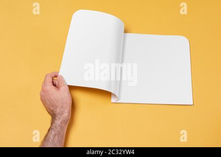 Männliche Hand öffnete einen Katalog auf gelbem Hintergrund, editierbare Modell-up-Serie Vorlage bereit für Ihr Design-Seiten Auswahl Pfad enthalten Stockfoto