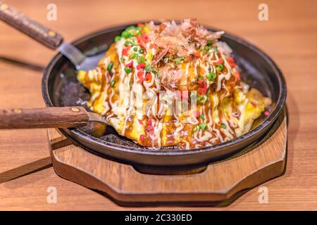 Japanische Okonomiyaki bedeckt mit Katsuobushi Lauch Mayonnaise und Bulldog-Sauce auf einem heißen Teller mit Spatel serviert. Stockfoto