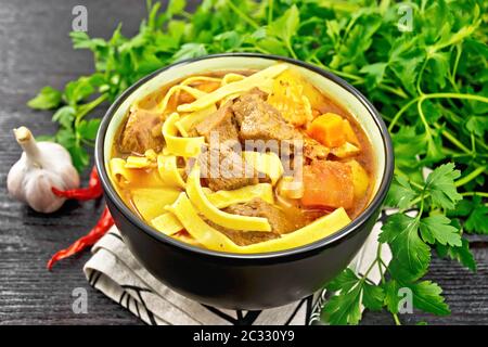 Zentralasiatisches Nationalgericht Lagman von Fleisch, Nudeln und Gemüse in der Schüssel auf einer Serviette, Knoblauch, Petersilie auf Holzbrett Hintergrund Stockfoto