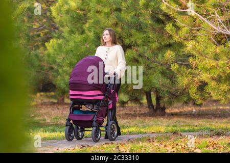 Mama spaziert mit Neugeborenem im Herbst-Stadtpark Stockfoto