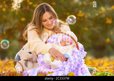 Mama schaut glücklich auf das zwei Monate alte Baby, das in einem Korb schläft, fliegende Seifenblasen Stockfoto