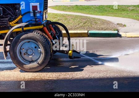 Blauer Traktor Bewässerung Asphalt für die Reinigung von Staub und Schmutz. Sommer Straßenreinigung Stockfoto