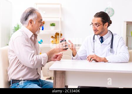 Junger männlicher Arzt besucht zu Hause den alten Patienten Stockfoto