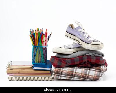 Stapel gefalteter Kleidung, Sport-Sneaker, Briefpapier auf weißem Hintergrund, Konzept zur Hilfe für Bedürftige, Spende Stockfoto