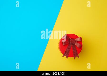Runde Karton Red Box mit einem Bogen auf einem blau-gelben Hintergrund, Ansicht von oben, Platz für Text Stockfoto