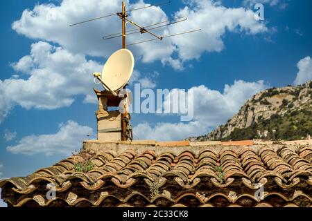 Eine alte Fernsehantenne und eine moderne Satellitenschüssel auf einem alten Lehmziegel-Pfeifendach Stockfoto