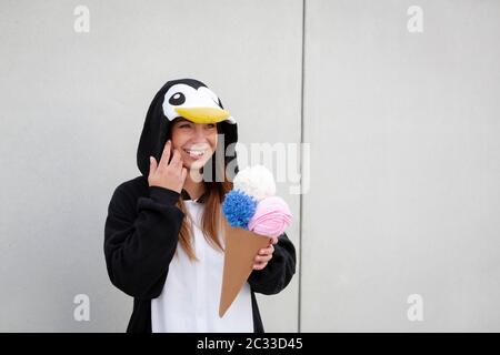Schöne, junge Frau in Pinguin Kostüm ist Essen deco Eis in der Betonwand Stockfoto