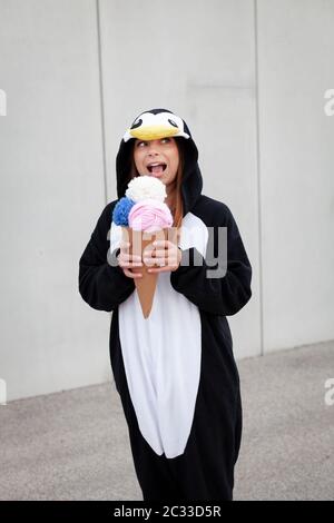 Schöne, junge Frau in Pinguin Kostüm ist Essen deco Eis in der Betonwand Stockfoto