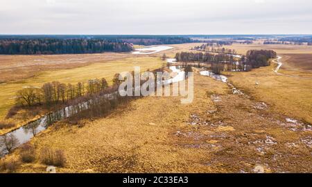 Kleiner Fluss mit trockenen Bäumen ohne Blätter im Winter / Frühfrühling Luftbild. Moody übergossen Wetter. Ackerland, Gärten und Felder in der Region Minsk, Stockfoto