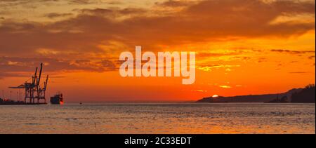 Sonnenuntergang in Ria de Pontevedra. Leuchtturm (Tambo) , zwei Frachtschiffe und Krane aus Marin Port zu sehen Stockfoto