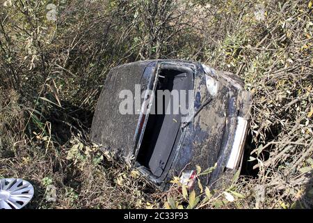 Totaler Autounfall auf dem Higway. Das Auto in den Büschen flog von der Bordsteinkante. Schwarzer Heckklappe ist nicht für die Rückgewinnung geeignet. Rückseite des Autos ohne Fenster. Stockfoto