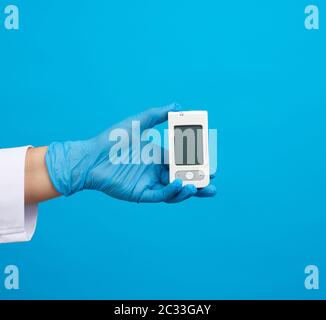 Hand in blau sterile Handschuhe halten ein weißes Blutzucker-Messgerät zur Messung von Blutzuckerwert, blauer Hintergrund Stockfoto