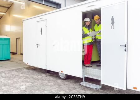 Arbeiter, die einen Toilettenwagen inspizieren, bevor er an den Kunden vermietet wird Stockfoto