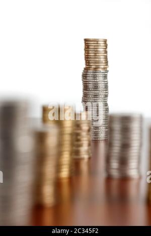 Flache, abgewinkelte Ansicht der gestapelten Euro-Münzen auf glattem Holzhintergrund. Mit Blende F8 auf den letzten Stapel fokussieren. Stockfoto