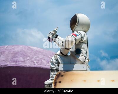 Ein Astronaut mit einem Schlauch von Lebensmitteln in der Hand sitzt auf dem Hintergrund des Himmels im Park von Russland Sotschi 06 22 2019 Stockfoto