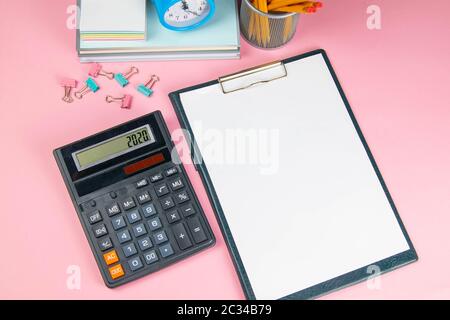 Auf dem rosa Tisch befindet sich ein Taschenrechner und ein Tablet mit einem weißen Blatt, neben gespritztem Wäscheklammern für Papier. Stockfoto