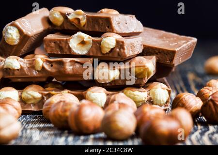 Ganze Haselnüsse im Schokoriegel, die Fliese ist gebrochen und liegt auf dem Holztisch Stockfoto