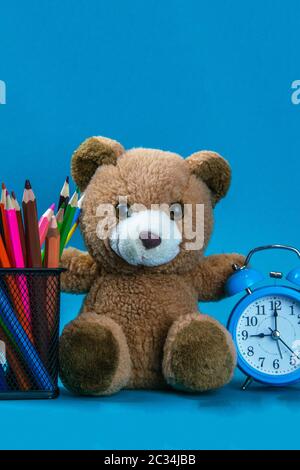 Blauer Wecker mit braunem Bär und Buntstift auf dem Holztisch platziert. Zeit zur Arbeit. Für Hintergrund und Textur verwenden. Stockfoto