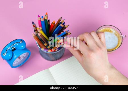 Tablette mit weißem Blatt, neben dem ist eine grüne Pflanze, ein Glas mit Bleistiften. Die Hand hält einen Stift und schreibt eine Uhr in eine andere Hand auf das Blatt. Stockfoto