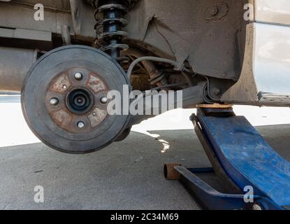 Altes und schmutziges Auto ohne Rad, Wagenheber mit hydraulischem Wagenheber für Reifen repariert, Nahaufnahme auf Scheibenbruch Stockfoto