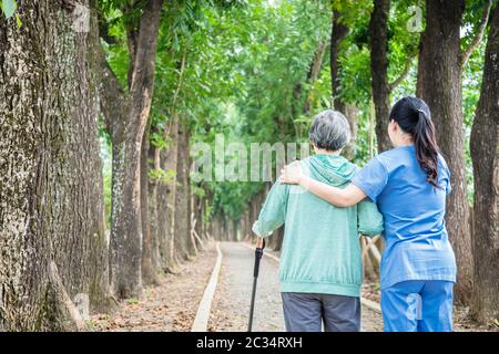 Lächelnd Krankenschwester helfen, ältere Frau, die rund um den Park zu Fuß Stockfoto