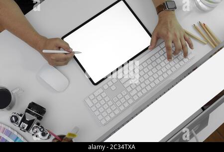 Aufnahme eines männlichen Fotografen mit einem Tablet-Modell auf dem Schreibtisch mit Computergeräten, Kamera und anderen Zubehörteilen Stockfoto