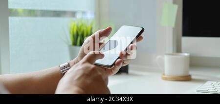 Nahaufnahme eines Geschäftsmannes mit einem Smartphone, während er am modernen Schreibtisch neben dem Fenster sitzt Stockfoto