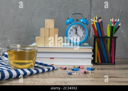 Ein Stapel Bücher, eine Uhr, Holzwürfel in Form einer Pyramide, daneben gibt es Tee mit Zitrone in einem transparenten Glas und bunten Penc Stockfoto