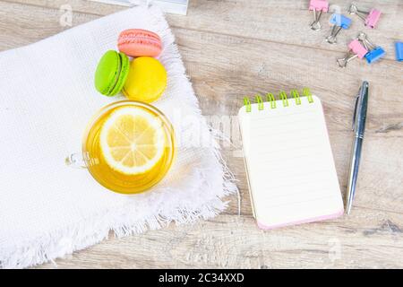 Daneben stehen ein offenes Notizbuch mit silbernem Stift, eine Tasse Minztee mit Zitrone und bunte Muffins. Stockfoto