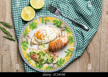 Englisches Frühstück, Rührei mit Wurst und Kohlsalat, daneben eine in zwei Hälften geschnittene Limette, ein Teller steht auf einem Holztisch. Stockfoto