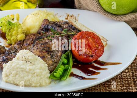 Steaks in Salbei und Apfelsauce mit Gemüse serviert.geröstete Rinderscheiben mit Beeren-, Apfel- und Birnensauce, Kartoffeln und grünem Salat Stockfoto