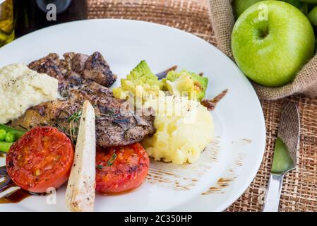 Steaks in Salbei und Apfelsauce mit Gemüse serviert.geröstete Rinderscheiben mit Beeren-, Apfel- und Birnensauce, Kartoffeln und grünem Salat Stockfoto